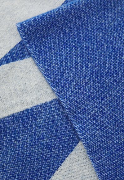 Textil albastru cu un model țesut, caracterizat de o textură moale. Marginea este cusută cu precizie, evidențiind diverse nuanțe de albastru pe un fond deschis.