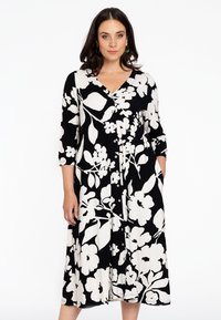 Sort-hvid blomsterkjole med V-udsk�æring, trekvartærmer, knaplukning foran og flared nederdel; stoffet har en glat tekstur.