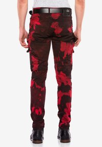 Rote und schwarze Batik-Cargo-Hosen mit mehreren Taschen, strukturiertem Stoff und körperbetontem Schnitt, kombiniert mit schwarzen Stiefeln.