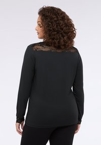 Maglia nera a maniche lunghe con dettagli in pizzo sulle spalle e sulle maniche; tessuto morbido; design aderente, indossata con leggings neri.