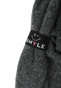 Dunkelgrauer Strickstoff mit einem schwarzen Etikett, auf dem ein zwinkerndes Smiley-Gesicht und das Wort "SMYLE" abgebildet sind, wobei das "Y" pink ist.