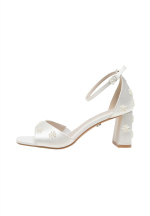 Sandales à talons en satin blanc avec bout ouvert, bride à la cheville et talon bloc ornées de motifs floraux sur les côtés et l'avant. Texture lisse.