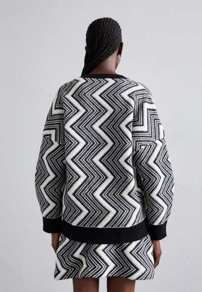 Wool blend sweater and skirt set featuring a striking zigzag pattern in black and white, with ribbed cuffs and hem. Textured finish, relaxed fit.