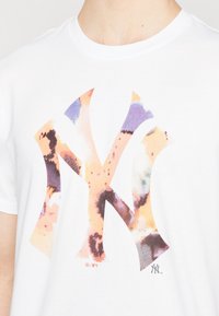 Camiseta blanca de manga corta con un gráfico del logo de NY multicolor con patrones en estilo acuarela y un cuello redondo.