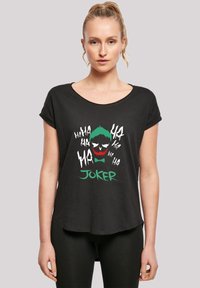 Svart T-skjorte med korte ermer som har et levende grafisk motiv av Joker med grønt hår, røde lepper, hvit tekst og en rund kant.