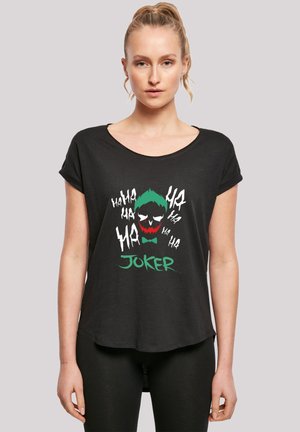 Svart T-skjorte med korte ermer som har et levende grafisk motiv av Joker med grønt hår, røde lepper, hvit tekst og en rund kant.