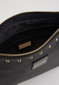 Clutch in pelle nera con accessori in oro, chiusura con zip e borchie metalliche. L'interno presenta un rivestimento con logo e una tasca con zip.