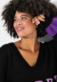 Maglione nero lavorato a maglia con scollo a V e accenti viola sulle maniche. Il tessuto sembra morbido, con una finitura testurizzata e polsini a coste.