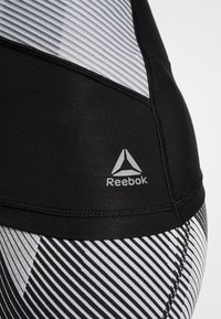 Närbild av svarta och vita randiga sportleggings och topp med Reebok-logotyp på det svarta midjebandet.