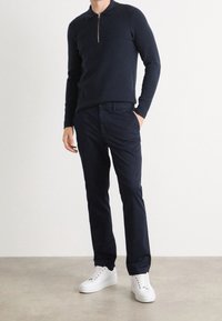 Polo shirt a zip con maglia blu navale abbinato a pantaloni blu navale e sneakers bianche. Focus sulla vestibilità sartoriale e sulla texture morbida dei materiali.