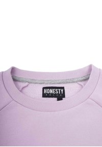 Lilac huppari, jossa on pyöreä kaula-aukko ribbidietaililla, pehmeä sisäosa ja musta lappu, jossa lukee "HONESTY RULES."