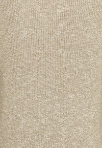 Tissu tricoté beige et blanc avec un motif côtelé texturé, montrant un gros plan des points.