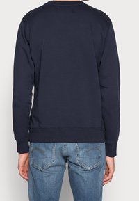 Felpa blu navy con maniche lunghe, colletto e polsini a coste, realizzata in tessuto morbido. Indossata con jeans in denim azzurri.