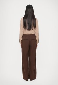 Beež pika varrukaga pluus nööpdetailidega varrukatel, kombineeritud pruunide laia säärega pükstega, millel on elastne vöökoht ja kaks tagataskut.