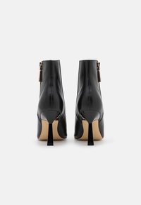 Botines de cuero negro con un diseño elegante, que cuentan con un tacón alto de aguja y un cierre de cremallera en el lateral. Textura suave, estilo minimalista.
