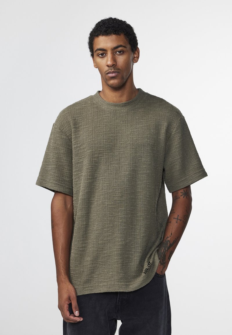 Oliven grøn kortærmet struktureret t-shirt med rund hals, der har en let løs pasform og synlige syninger langs kanten.