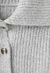 Cárdigan gris claro de punto con textura acanalada, que presenta un cuello ancho y un detalle destacado de botones en el frente.