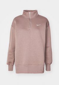 Ljust rosa Nike-tröja med hög krage och halv dragkedja. Har sänkta axlar och ribbade ärmslut och nederkant. Enkel logotyp i vitt.