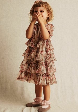 Lagdelt kjole i blomstermønster, med rynkede lag i blød beige, med korte ærmer. Sat sammen med grå flade sko og lyserøde, frynset sokker.