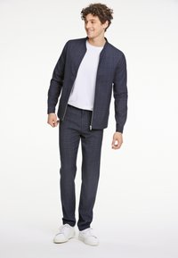 Marinblått kavaj- och byxset med rutmönster i texturerad tyg, med dragkedja och kombinerat med vita sneakers.