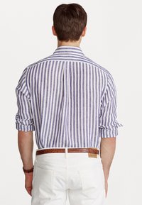 Randig skjorta i lila och vit linne med knappar och uppvikkta ärmar. I kombination med vita byxor och ett brunt texturerat bälte.