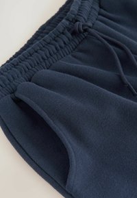 Shorts en molleton bleu marine avec taille élastique, cordon de serrage et poches latérales. Texture douce avec une finition lisse et sans motifs visibles.