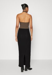 Haut à bretelles marron associé à une jupe longue noire côtelée avec une fente latérale, complété par des bottines à talons blocs noires.