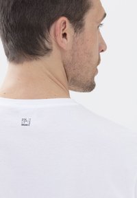 Camiseta blanca de algodón con un escote redondeado y una pequeña etiqueta impresa en la parte posterior que dice "NO TE PREOCUPES, ES ORGÁNICO."