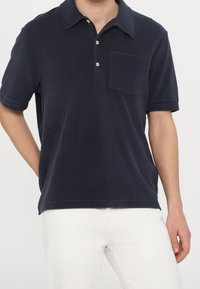 Polo azul marino confeccionado en una tela suave, con cuello, tres botones y un bolsillo en el pecho. Mangas cortas y corte relajado.