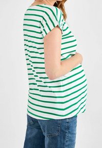 Camiseta de rayas de manga corta en verde y blanco, con un corte holgado y cuello redondo, combinada con pantalones de mezclilla azules.