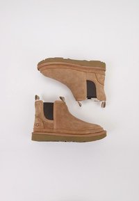 Botas de tobillo de ante marrón con paneles laterales elásticos, suela de goma texturizada y tiradores en el talón. Detalles de costura reforzada.