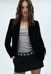 Sort fløjl blazer med skræddersyet pasform, båret over en grå tanktop, parret med en sort miniskørt med sølvnitter langs taljen.