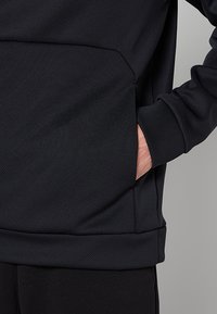 Czarny sweatshirt z teksturowanej tkaniny, z kieszenią z przodu i dzianinowymi mankietami. Projekt podkreśla minimalistyczny styl oraz praktyczność.