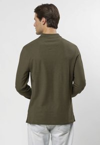 Långärmad polo i olivgrönt med hög krage och slät yta. Sömdetaljer på baksidan, med rak fåll och sidventilationer.
