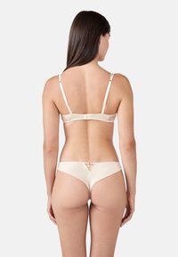 Ensemble de lingerie en satin beige comprenant un soutien-gorge avec des bretelles réglables et un string avec un détail découpé au dos. Texture lisse sur l'ensemble.