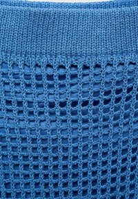 Tissu tricoté bleu présentant un motif texturé en mailles ouvertes avec de plus grandes découpes carrées. Le bord supérieur est tricoté plus serré.