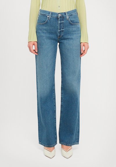 Modre kavbojke z visokim pasom in širokimi hlačnicami iz srednje obarvanega denima s klasičnim dizajnom s petimi žepi in subtilnim bledenjem, kombinirane s koničastimi belimi petami.