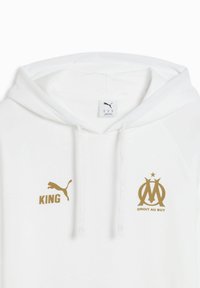 Hvid hoodie med guld "PUMA" logo, "KING" tekst og "OM" emblem med stjerne. Blødt materiale med snoretræk i hætten og ribbede detaljer.
