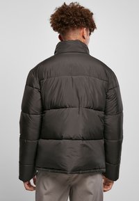 Dunjakke i mørkegrå med høj krave, quilted design og elastiske manchetter. Glat, blank overflade med løs pasform.
