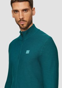 Teal ritsvest met een hoge kraag, geribbelde textuur en een vierkante logo patch op de borst. Ontworpen met een getailleerde Silhouette.