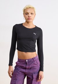 Top cropped preto de manga longa com decote redondo e logo branco da Puma. Combinado com calças cargo roxas de cintura alta com bolsos.