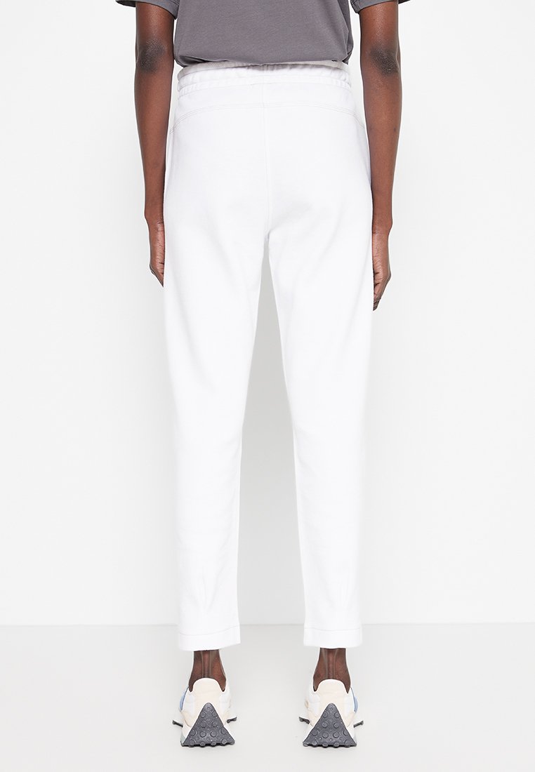Weiße Jogginghose mit schmaler Passform, elastischem Bund und Seitentaschen, kombiniert mit hellen Sportschuhen mit texturierten Sohlen.