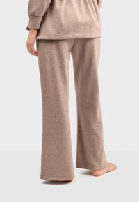 Brązowe, miękkie spodnie dresowe o luźnym kroju i rozszerzanych nogawkach, z elastycznym paskiem w talii i subtelną strukturą na całej powierzchni.