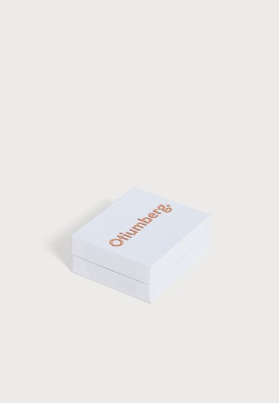 Une boîte à bijoux rectangulaire blanche, avec un couvercle texturé et le mot « Otilumberg » en lettres couleur cuivre, sur un fond uni.