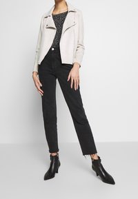 Jasnoszara kurtka motocyklowa ze skóry zamszowej na wzorzystą bluzkę, zestawiona z czarnymi, wysokim stanem jeansami i czarnymi botkami na szpic.