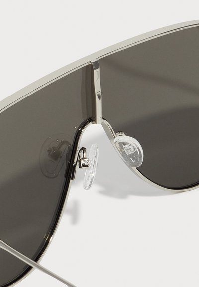 Silver metal sunglasses with dark grey lenses, featuring a wide frame, nose pads, and a bridge detail. Smooth, reflective finish.