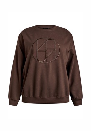 Pruun pusa, mis on valmistatud pehmest kangast ja millel on tumedama tooniga ümmargune logo. Sellel on ümar kaelus ja soonikkoes varrukate otsad.