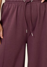 Lila Sweatpants mit einem elastischen Bund und verstellbarem Kordelzug. Weiche Textur mit geradem Bein und silbernen Hardware-Details.