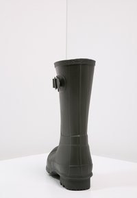 Schwarzer Gummistiefel mit strukturierter Oberfläche, geradem Schaft und einer kontrastierenden Schnalle an der Rückseite. Mit flacher Sohle und Profil.
