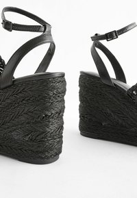 Schwarze Keilsandalen mit einem geflochtenen Seilabsatz, Lederriemen und einer verstellbaren Knöchelschließe. Texturiertes Design für zusätzlichen Halt und Stil.